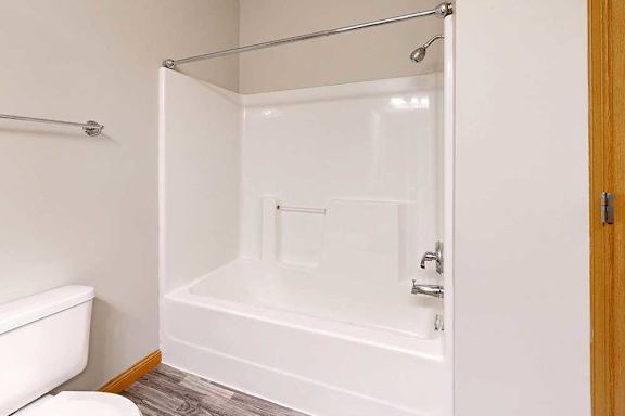 A bathroom with a white tub shower with chrome finishes..