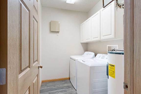A laundry room with hard wood flooring, full-sized washer and dryer, and four overhead storage cabinets.