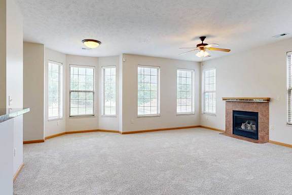 A living room with a tiled fireplace, a bay window, several other tall windows for plenty of natural light, and a ceiling fan light.