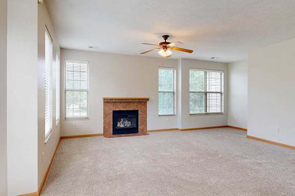 A living room with a tiled fireplace, several tall windows, and a ceiling fan light.