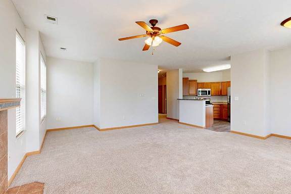 A living room with a ceiling fan and a kitchen in the background.