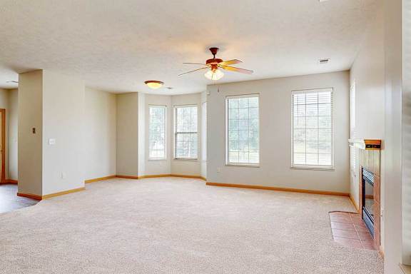 A spacious living room with several windows, a tile fireplace, and a ceiling fan.