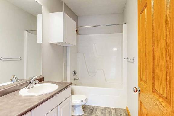 A bathroom with a vanity sink, overhead storage cabinets, and tub shower.