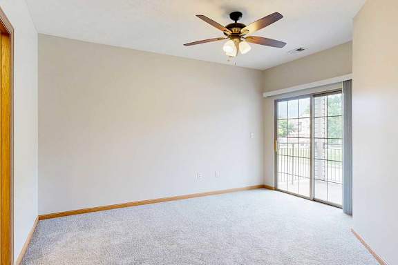 A primary bedroom with a sliding glass door to the balcony, a ceiling fan, and an attached bathroom.
