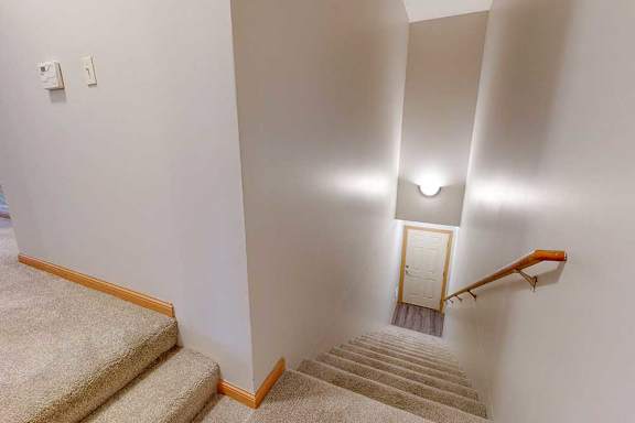 A carpeted staircase with a wooden handrail leading up from a tiled foyer at the front private entry.