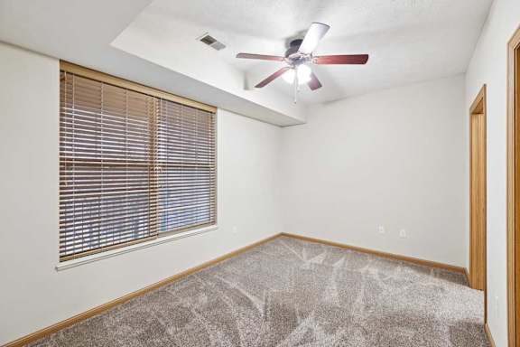 Bedroom with large window, ceiling fan, and neutral carpet.