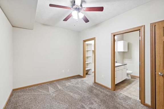 Bedroom with ceiling fan and open access to bathroom and hallway.