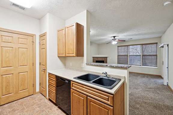 Kitchen with natural wood cabinets, double-basin sink, laminate countertops, and breakfast bar overlooking living area.