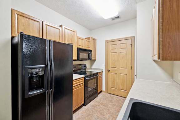 A kitchen with a black refrigerator, microwave, oven and sink.