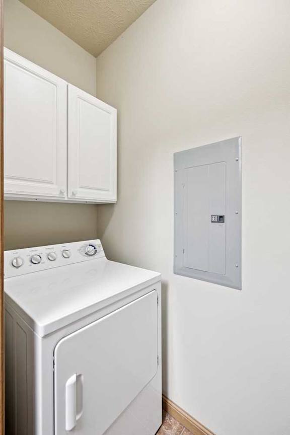 In-unit laundry area with dryer, white upper cabinets, and tile flooring.