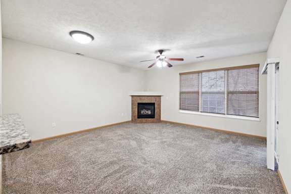Bright living room with large window, ceiling fan, and corner fireplace.