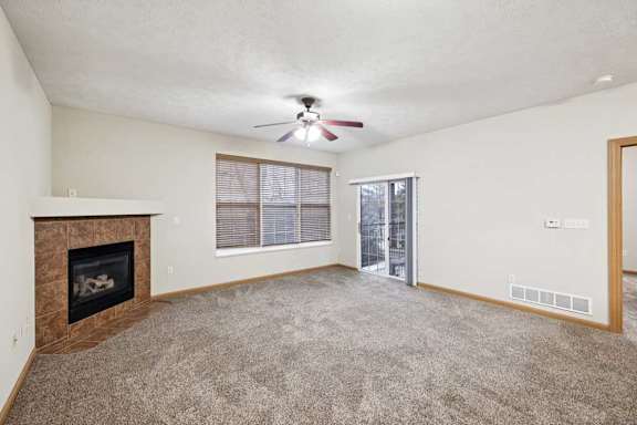 Spacious living room with plush carpet, ceiling fan, corner fireplace, and sliding glass door to balcony.