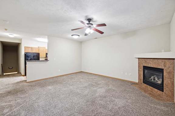 Open living and dining area with ceiling fan, plush carpet, and fireplace with tile surround.