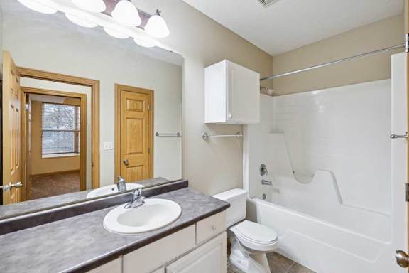 Full bathroom with single-sink vanity, large mirror, white cabinetry, and tub-shower combo with built-in surround.