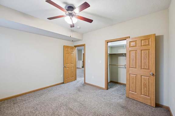 Carpeted bedroom featuring ceiling fan, double-door closet, and natural wood trim throughout the apartment interior.