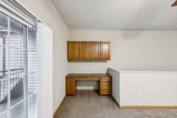 Built-in desk area with upper cabinets and granite-look countertop, located near sliding door to the balcony.