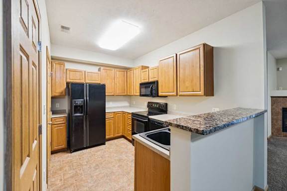 Apartment kitchen with wood cabinetry, black refrigerator, oven, microwave, and breakfast bar with raised counter.