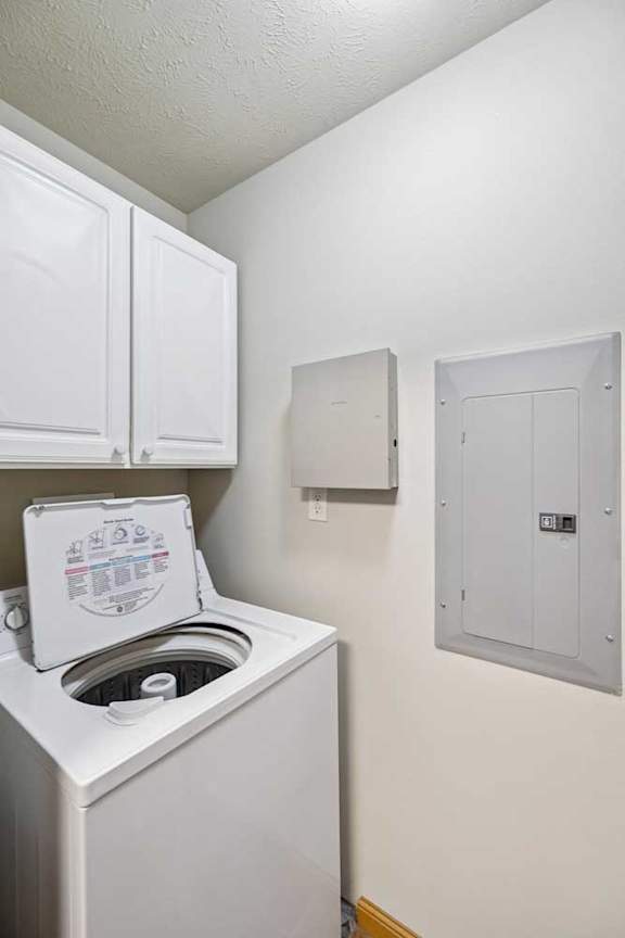 Laundry closet with top-load washer, dryer, and adjacent electrical panel inside the apartment.