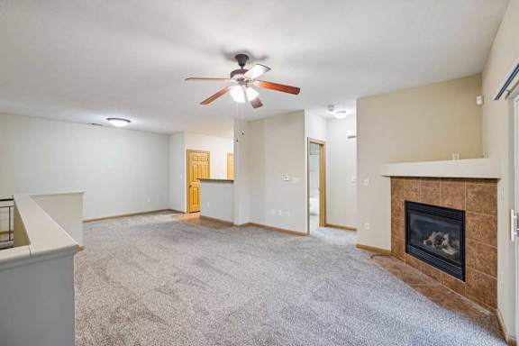 Spacious living room with plush carpet, ceiling fan, tile-surround fireplace, and open layout to kitchen.