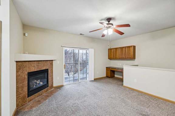 Living room with corner fireplace, ceiling fan, and built-in desk nook near balcony access.