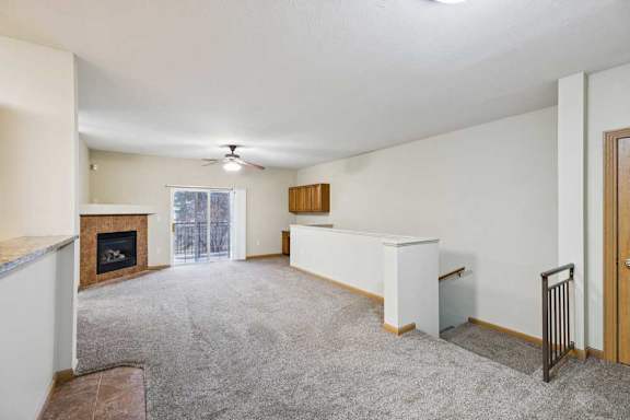Open-concept apartment living room with tile-surround fireplace, sliding glass door to balcony, and stair railing leading downstairs.