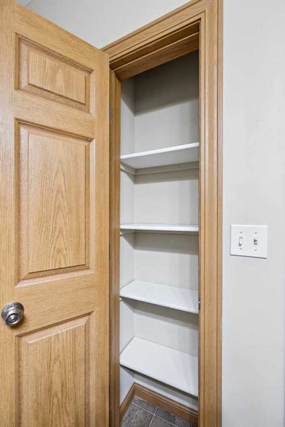 Linen closet with built-in white shelving and wood trim, offering convenient storage space inside the apartment.