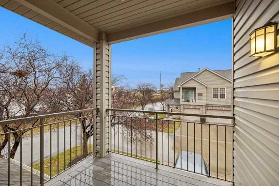 Covered upper-level balcony with wood-look flooring, metal railing, and neighborhood views.