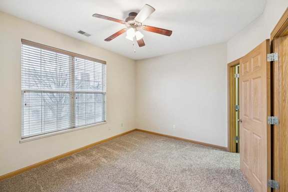 Bedroom with plush carpet, large window with blinds, ceiling fan, and neutral finishes.