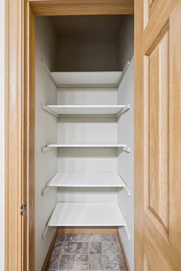 A white pantry with shelves and a tile floor.