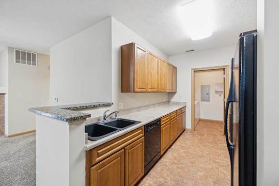 Kitchen with natural wood cabinets, laminate countertops, double-basin sink, black dishwasher, and adjacent laundry room access.