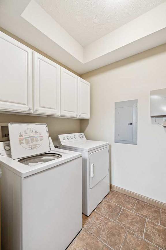 In-unit laundry room with washer and dryer, white upper cabinets, and tile flooring.