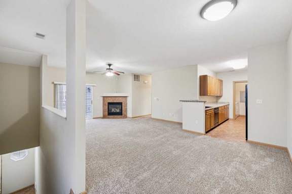 Open-concept living area with plush carpet, fireplace with tile surround, and kitchen with breakfast bar.