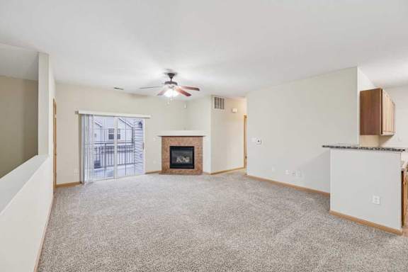 Open living room with plush carpet, ceiling fan, sliding glass door to private balcony, and corner fireplace with tile surround.