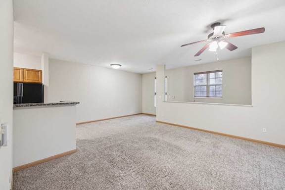 Open-concept living and dining area with plush carpet, ceiling fan, breakfast bar, and neutral finishes throughout.