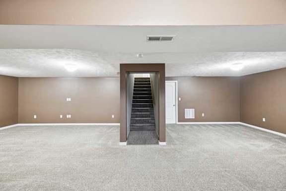 Finished lower-level family room with carpet flooring, recessed lighting, and central staircase access.