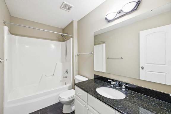 Full bathroom with tub/shower combo, granite vanity countertop, and tile flooring.