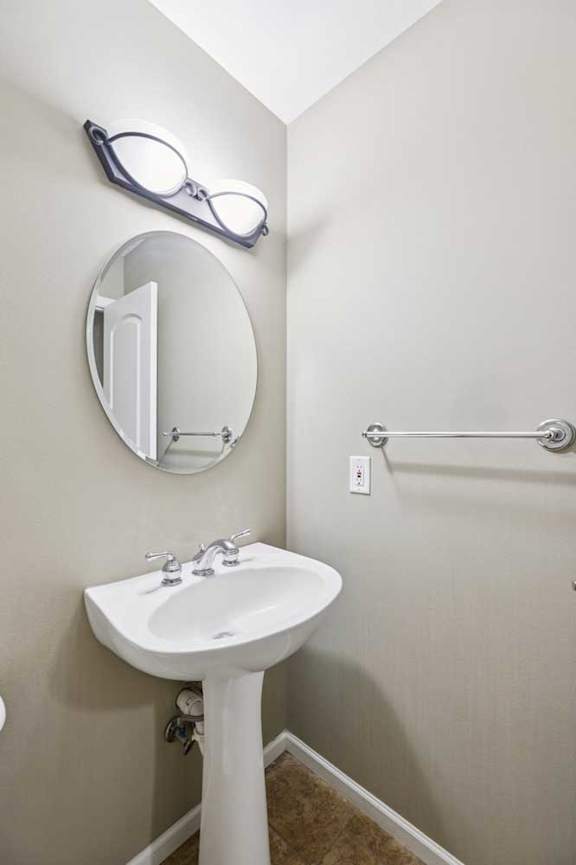 Half bathroom with pedestal sink, oval mirror, and tile flooring.