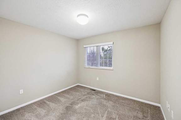 Secondary bedroom with neutral carpet, ceiling light, and window with blinds.