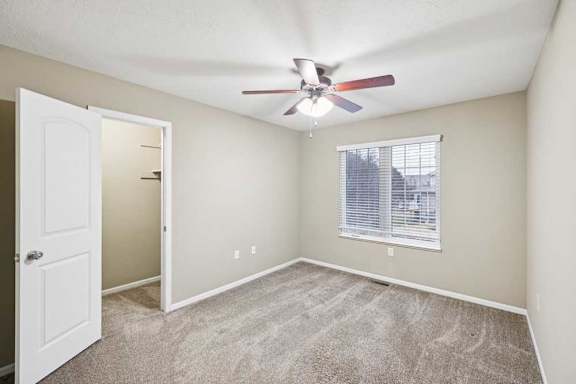 Secondary bedroom featuring ceiling fan, large window with blinds, and dual closets.