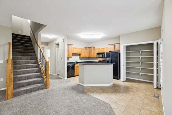 Open-concept apartment living area with carpeted stairs, tile kitchen flooring, peninsula breakfast bar, and walk-in pantry with built-in shelving.