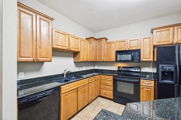 U-shaped kitchen with natural wood cabinets, black granite countertops, black appliances, and double-basin sink.