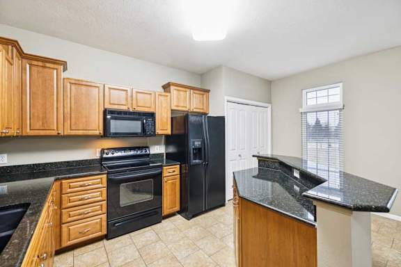 Kitchen with peninsula bar seating, oven and microwave, side-by-side refrigerator, and window for natural light.