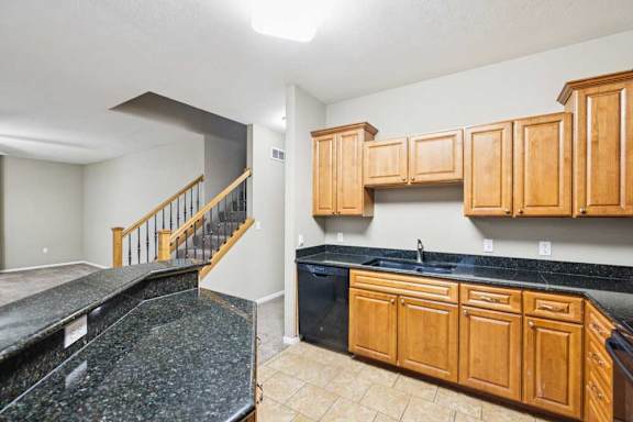 Kitchen and stair view showcasing granite counters, dishwasher, and open layout to living space.