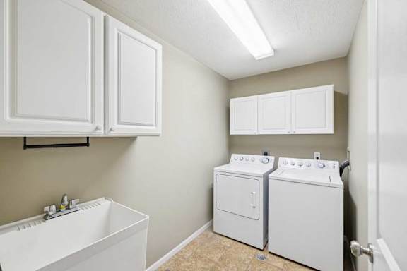In-unit laundry room with washer and dryer, utility sink, and overhead storage cabinets.