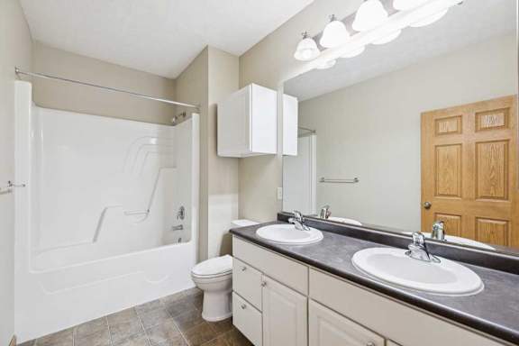 Full bathroom with double-sink vanity, large mirror, overhead lighting, tub and shower combination, and tile-look flooring.