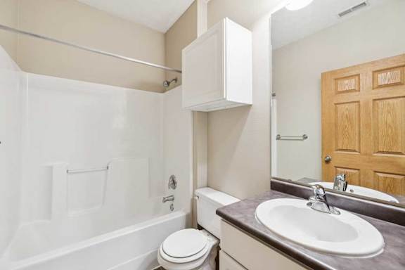 Bathroom with single-sink vanity, wall cabinet, mirror, and tub and shower combination with built-in surround.