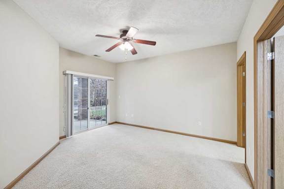 Spacious bedroom with plush carpet, ceiling fan, and sliding glass door leading to a private patio.