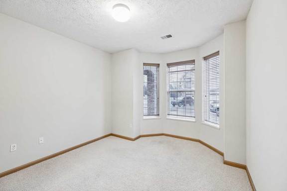 Bright bedroom with bay-style windows, neutral carpet, and wood trim for a clean apartment interior.