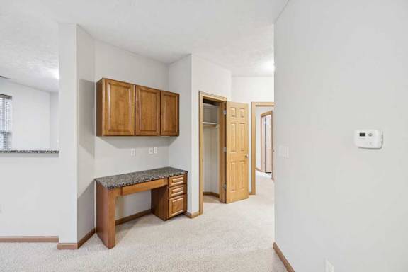 Living area with built-in desk and upper cabinets, laminate countertop, and open access to hallway and bedrooms.