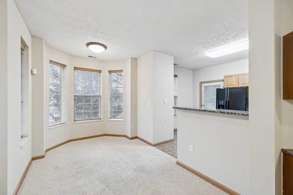 Open dining area with bay windows, neutral carpet, and breakfast bar overlooking the kitchen.